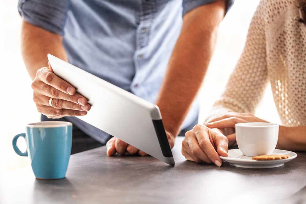 Man showing a woman digital financial planning tools on a tablet while they both enjoy coffee