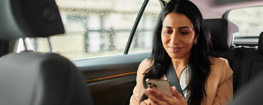 Businesswoman in car, checking the markets on her smartphone.