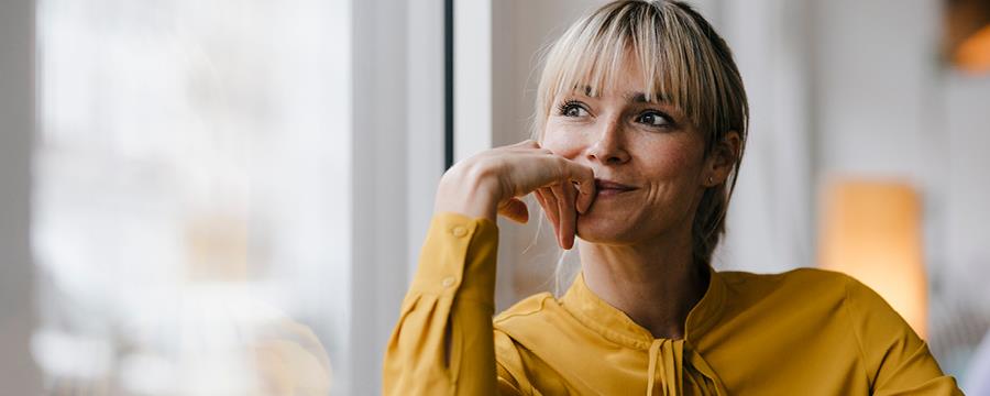Blond woman in yellow shirt looking out a window pensively