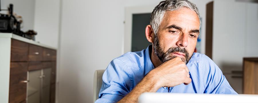 Man in his home office contemplating a question while looking at his computer