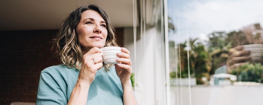 Contemplative mature woman looking through the window at home.