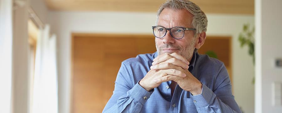 Mature man with eyeglasses looking out the window at home.