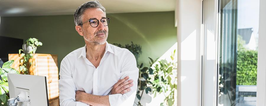 Businessman with arms crossed leaning on desk at home office.