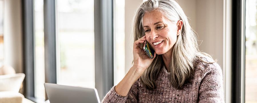 Woman talking on her smratphone and using her latpop at home.