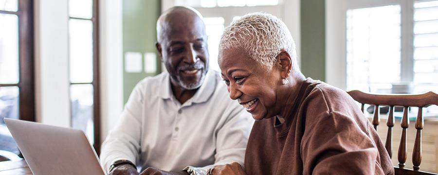 Happy retired couple looking at laptop at kitchen table.
