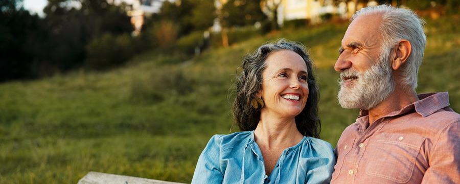 A married couple sitting on a bench outside, smiling.