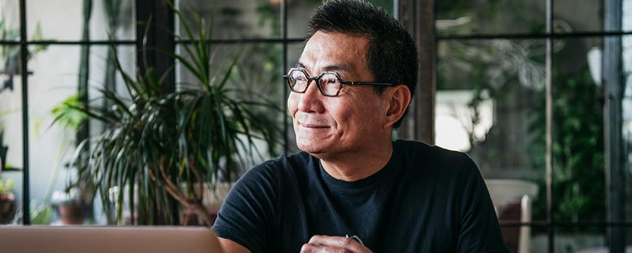 Cheerful man, sitting at table with laptop, looking away