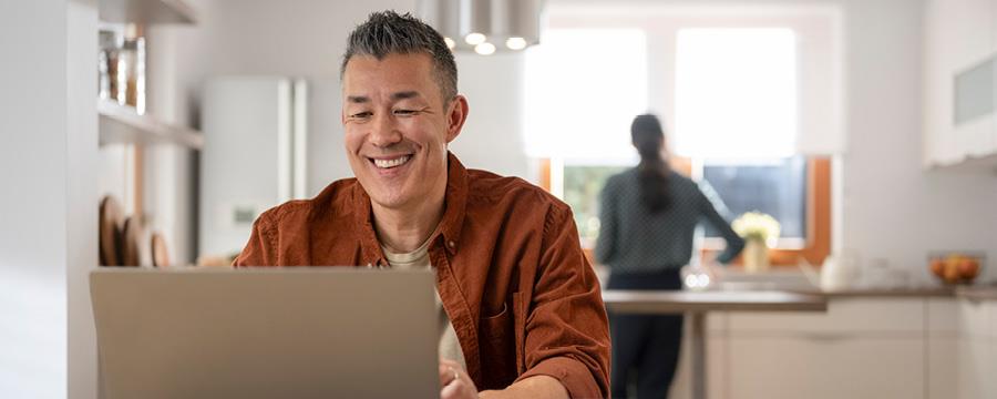 Happy man looking at his laptop, while sitting at the kitchen table.